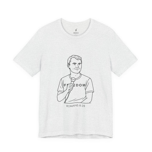 White t-shirt with black line art of Charlie Kirk holding a microphone and text 'Freedom Romans 8:28' on a white background