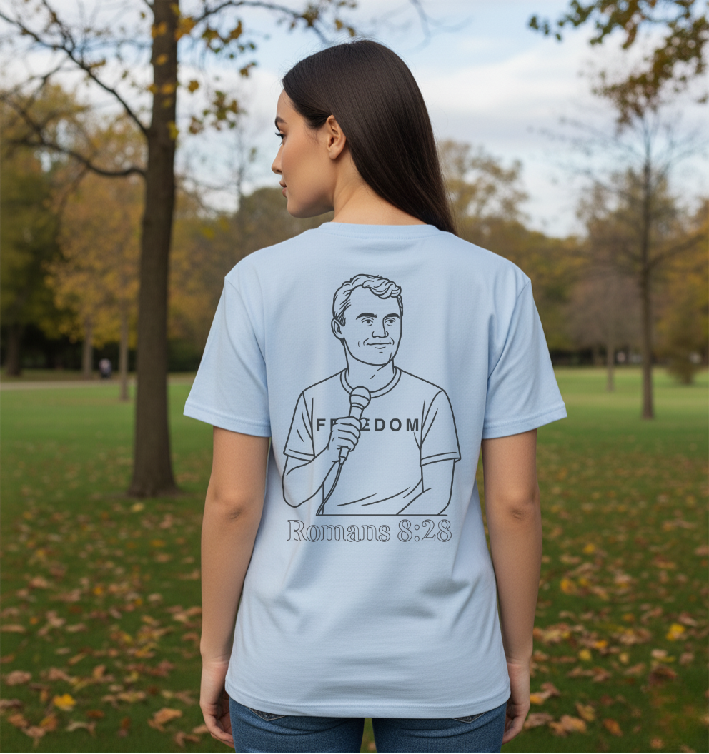 Person wearing a light blue t-shirt with a graphic and text in a park