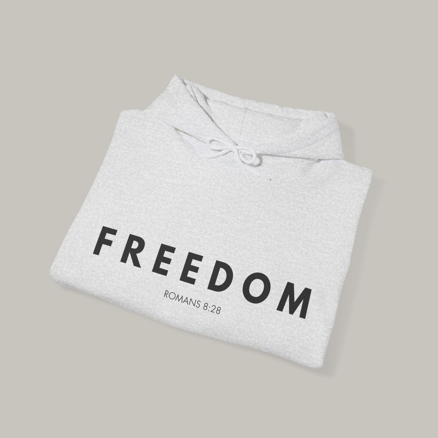 Folded gray hoodie with 'FREEDOM ROMANS 8:29' text on a beige background