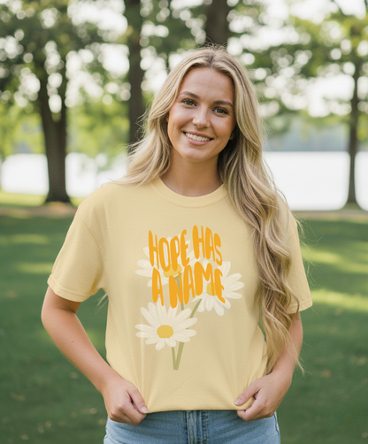 Woman wearing a yellow t-shirt with a floral design and text outdoors.