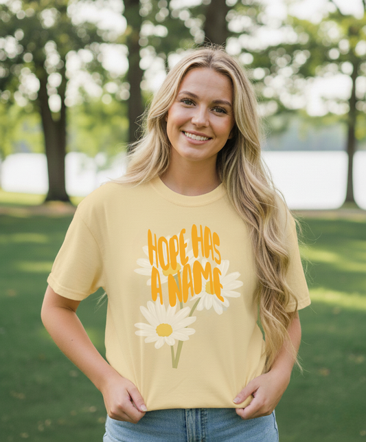 Woman wearing a yellow t-shirt with a floral design and text outdoors.