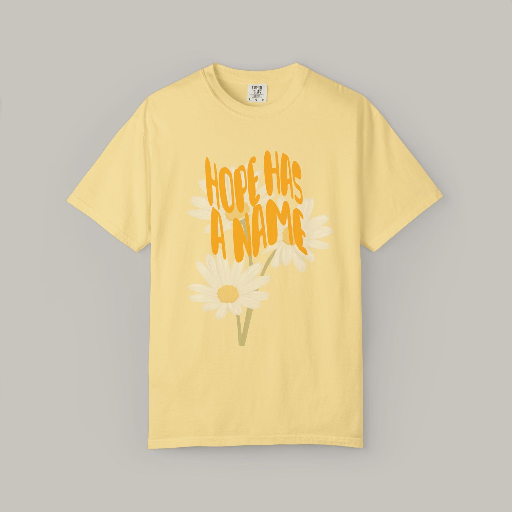 Yellow t-shirt with 'Hope Has a Name' text and daisy graphics on a gray background