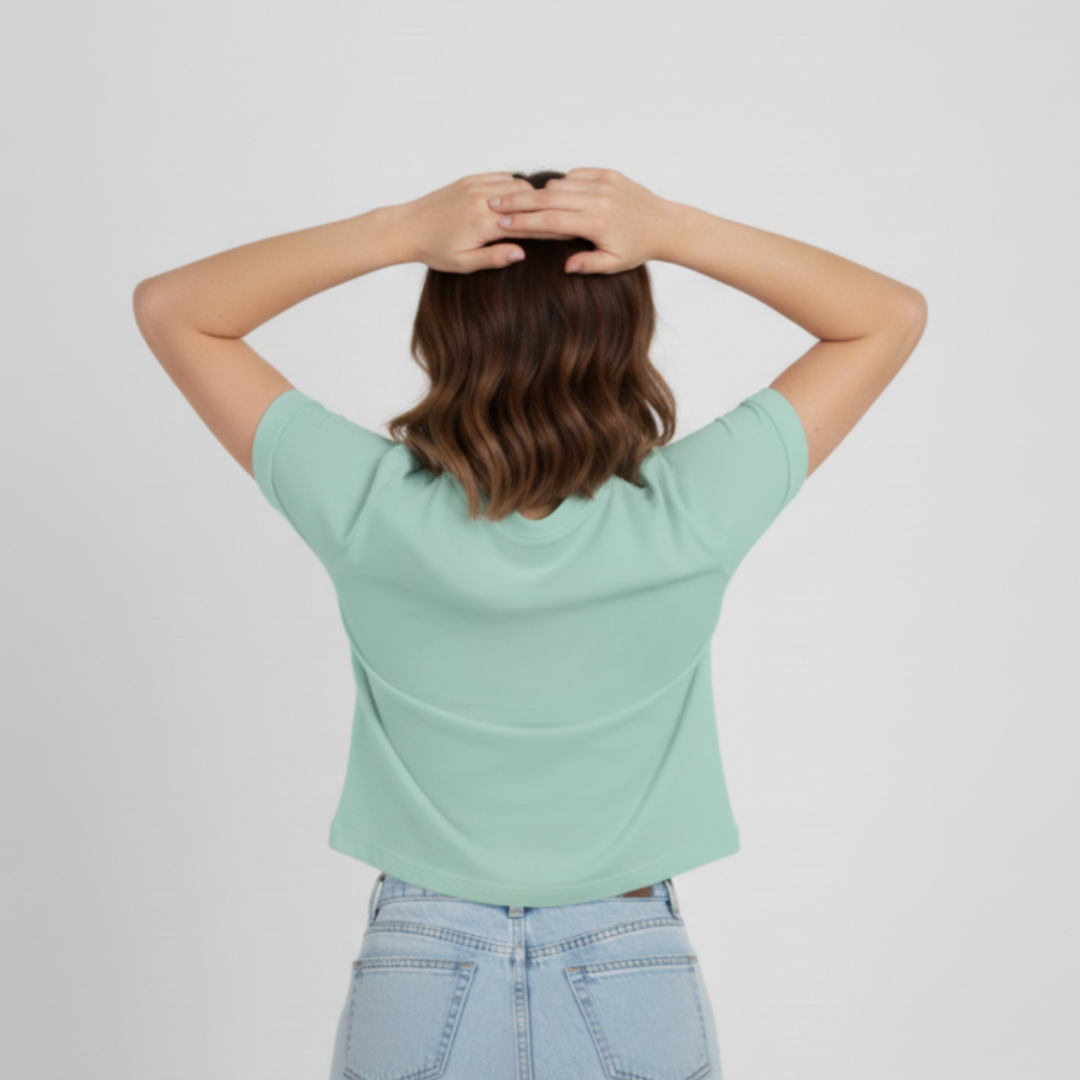 Person wearing a light green t-shirt and light blue jeans with hands behind head on a plain background