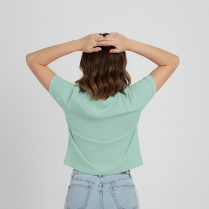 Person wearing a light green t-shirt and light blue jeans with hands behind head on a plain background