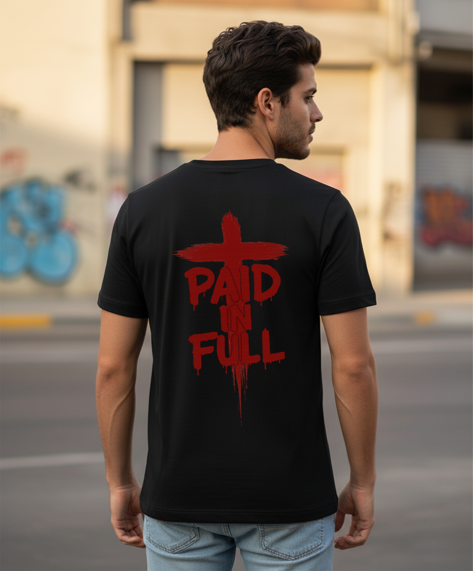 Man wearing a black t-shirt with red text 'PAID IN FULL' on the back, standing on a street.